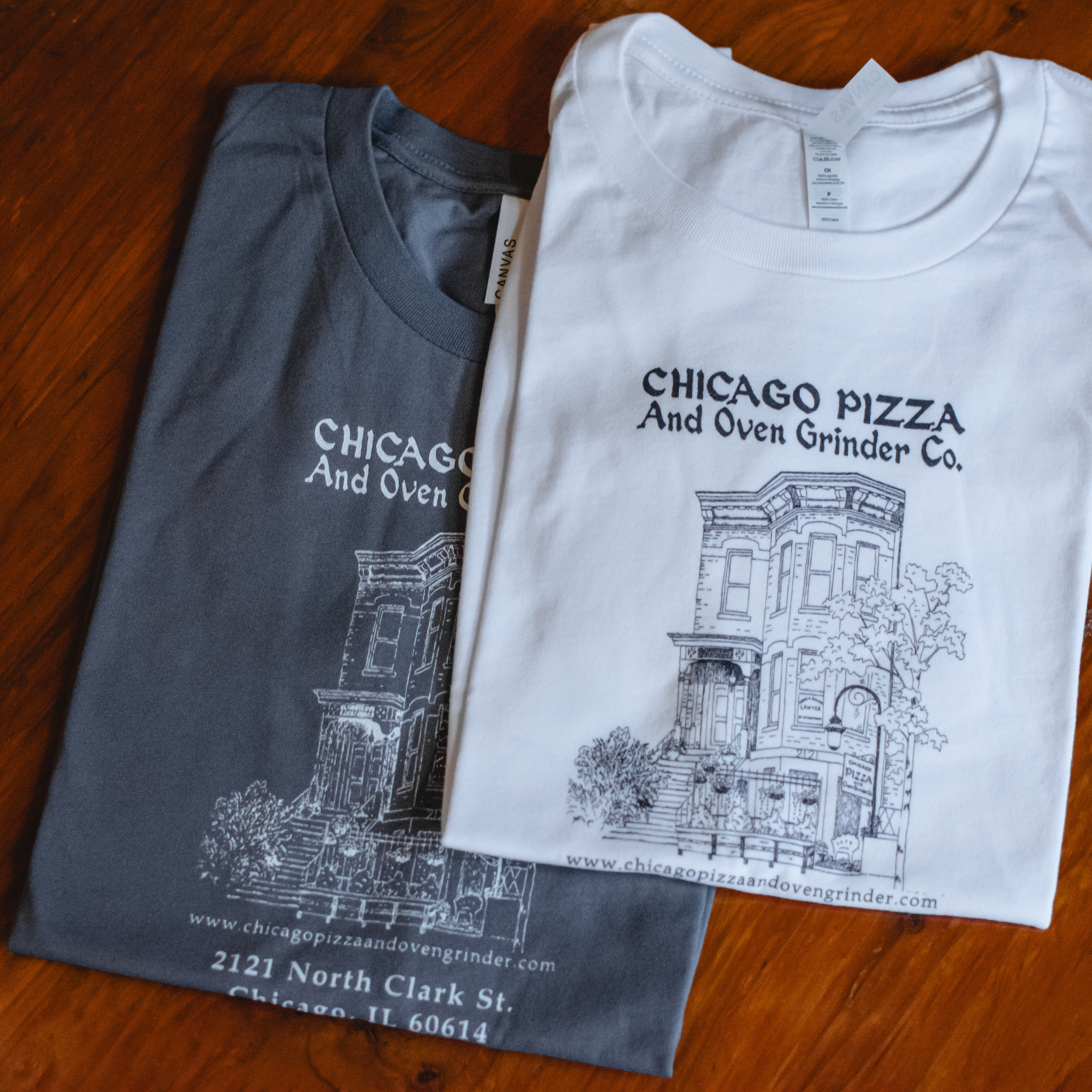 Two folded t-shirts with architectural design and text on a wooden surface