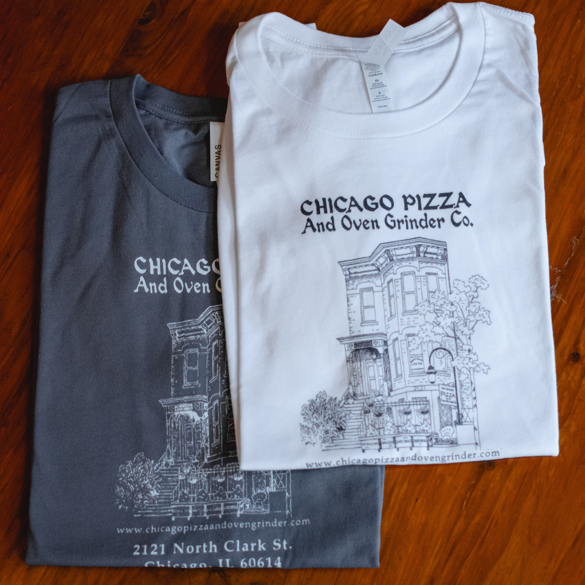Two folded t-shirts with 'Chicago Pizza and Oven Grinder Co.' design on a wooden surface