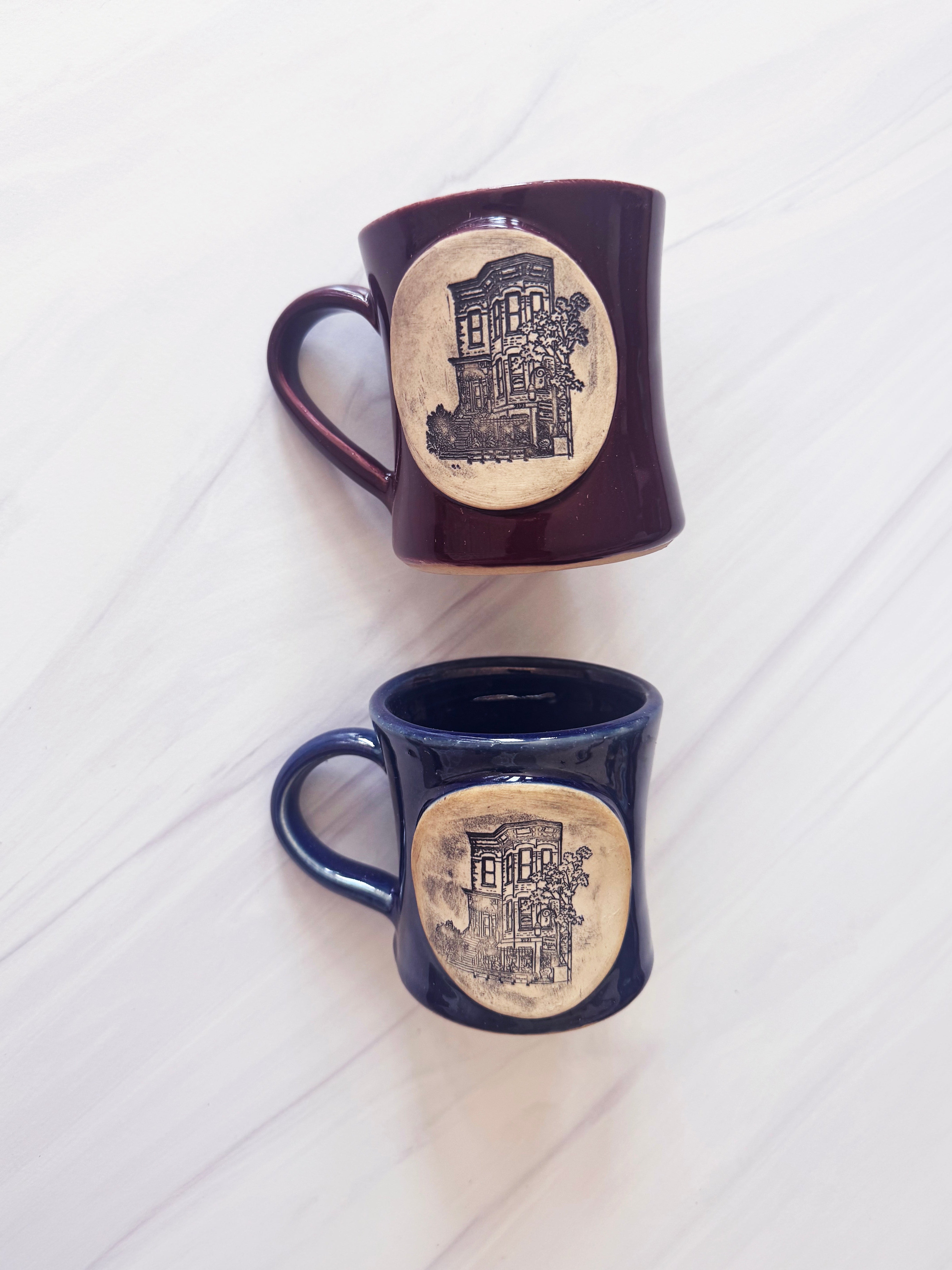 Two mugs with decorative designs on a white wooden surface